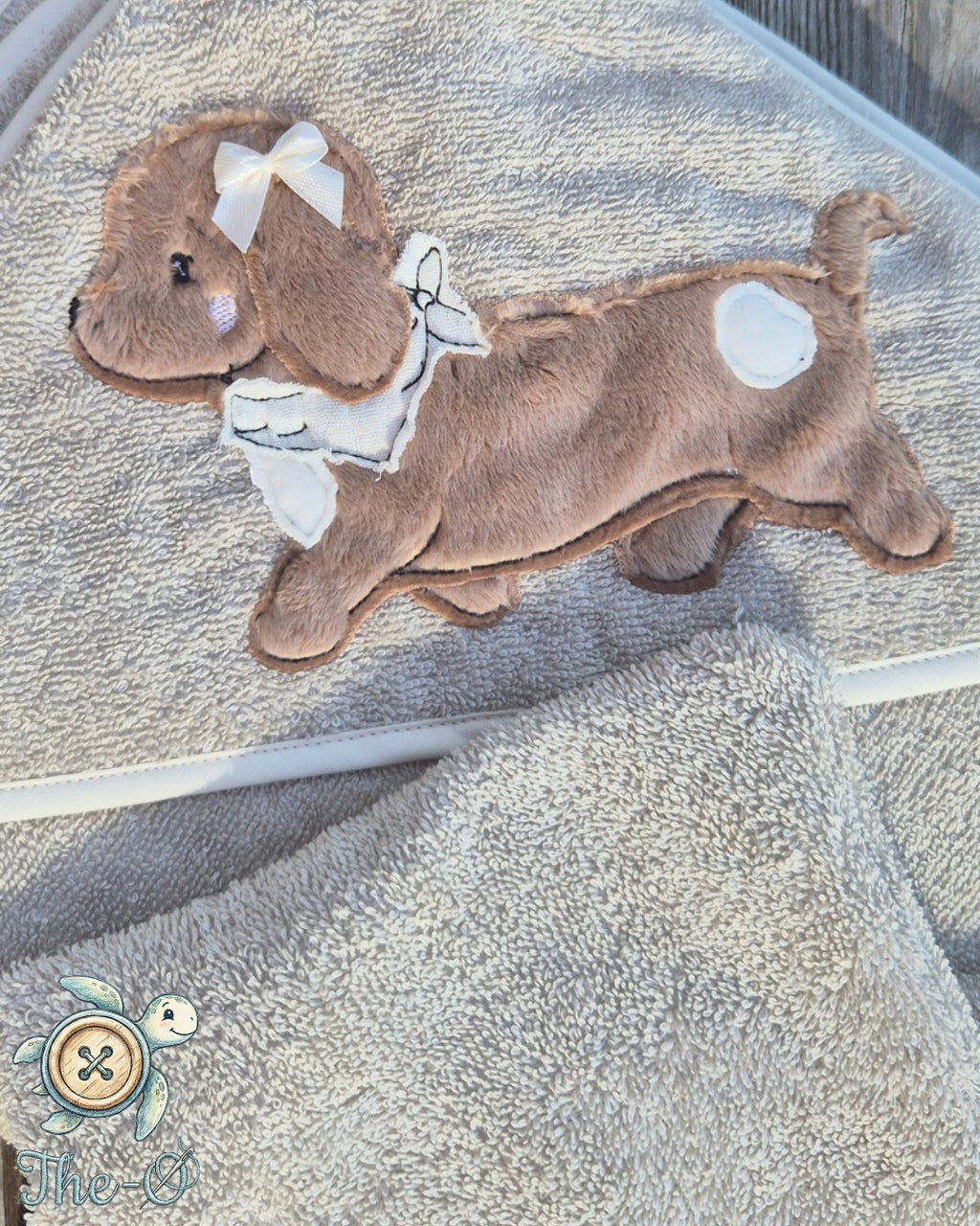 The-O Dackel Set bestehend aus beigem Handtuch und Waschlappen mit weicher Dackel-Applikation und weißer Schleife