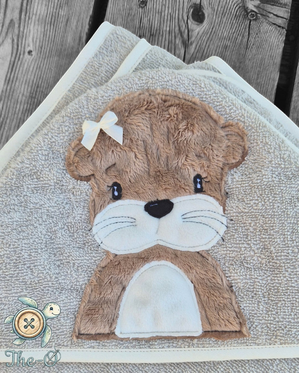 The-O Otter Set bestehend aus beigem Handtuch und Waschlappen mit flauschiger Otter-Applikation und kleiner Schleife